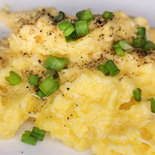 A closeup of creamy scrambled eggs with green onions on a white plate