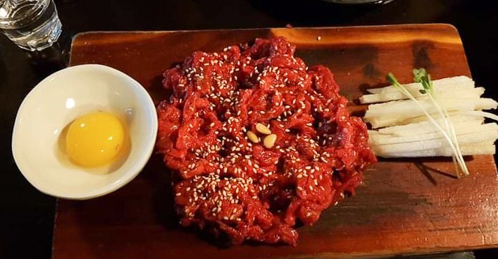 Beef tartare on a wooden plate with slices of Korean pear and a raw egg yolk in a bowl