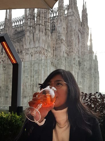 A woman drinking an Aperol spritz on a terrace overlooking the Duomo in Milan, Italy