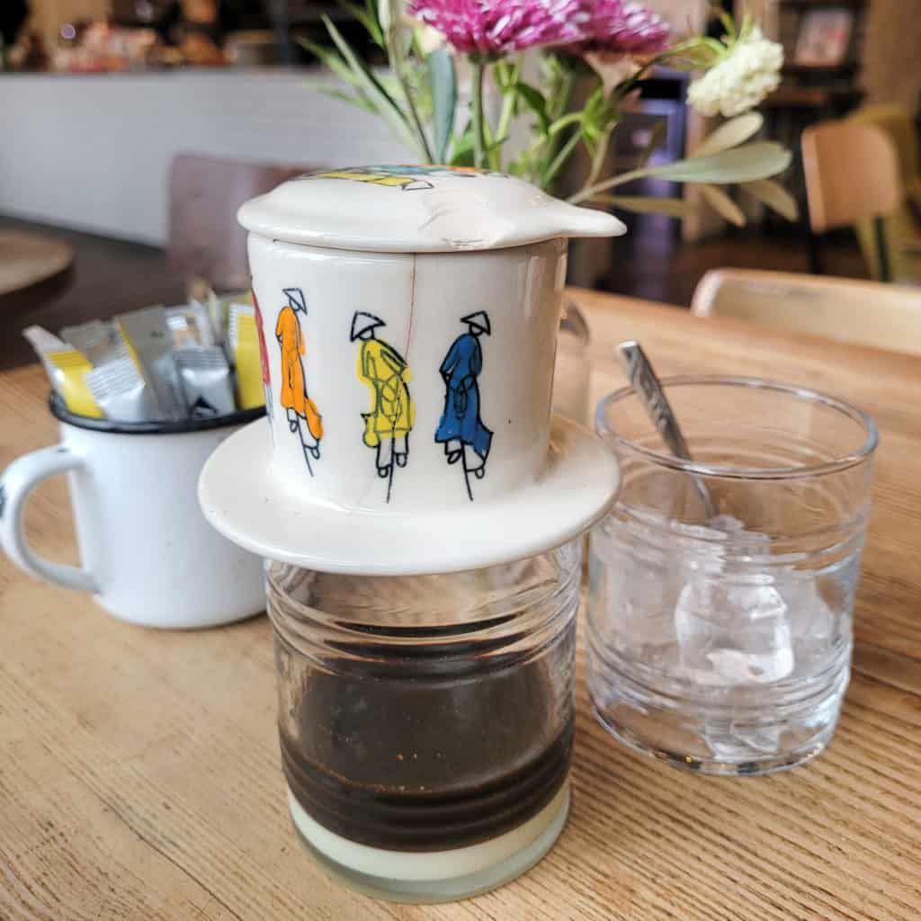 Porcelain Vietnamese coffee filter on top of clear glass on table in front of flowers