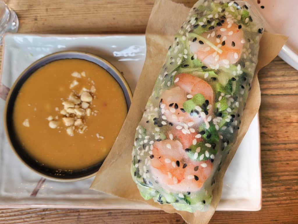 Vietnamese spring roll with lettuce and shrimp next to peanut sauce on a square plate