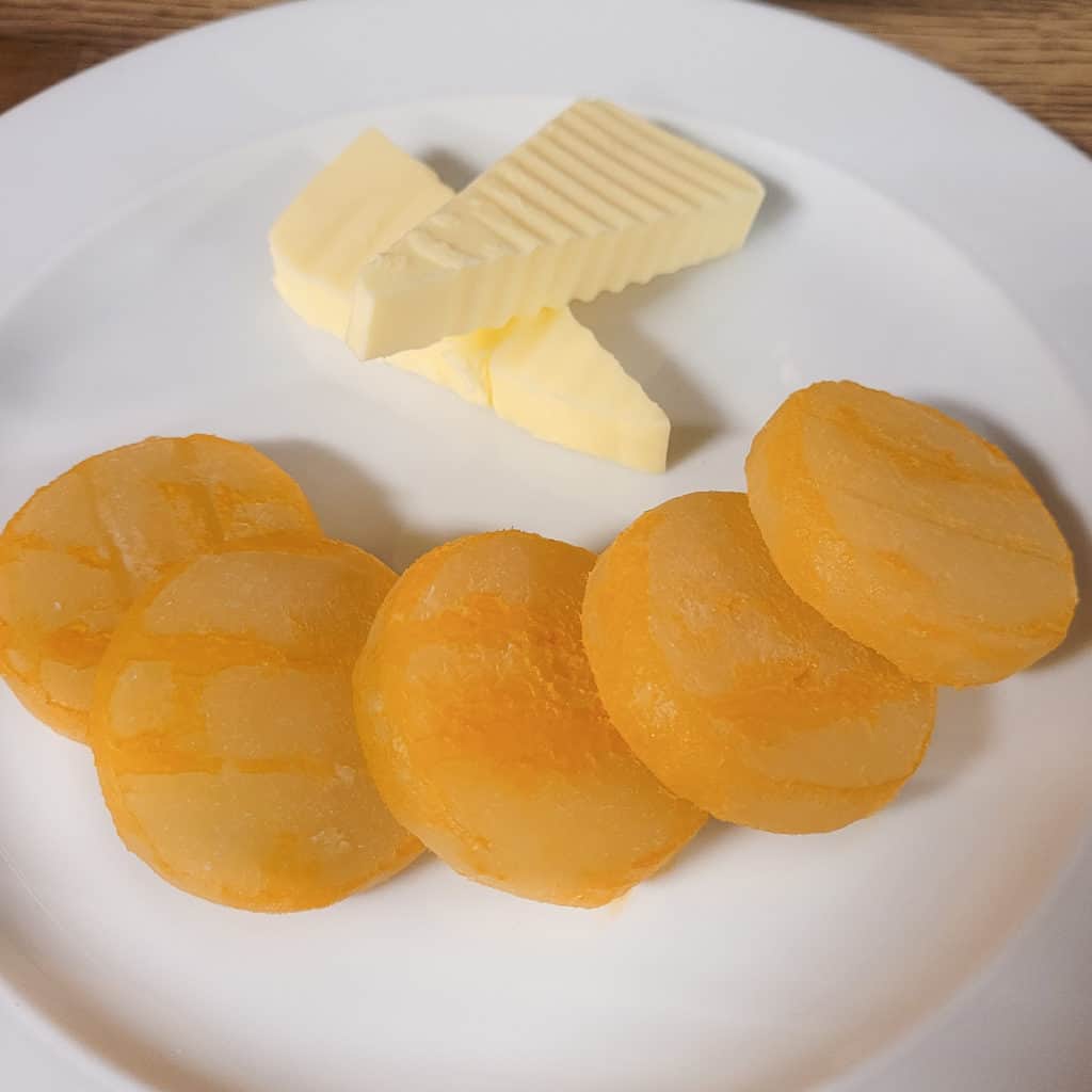 A plate of cheese that is round and orange served alongside butter shaped in triangles