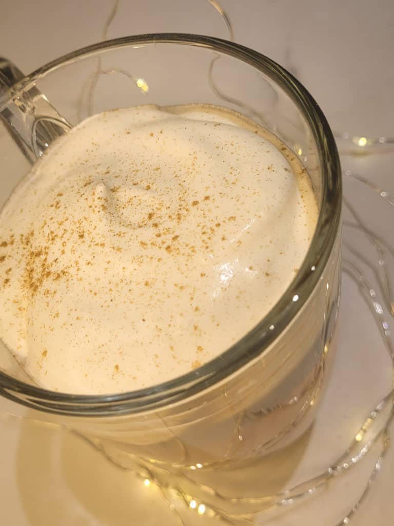 A clear mug with whipped cream surrounded by string lights.