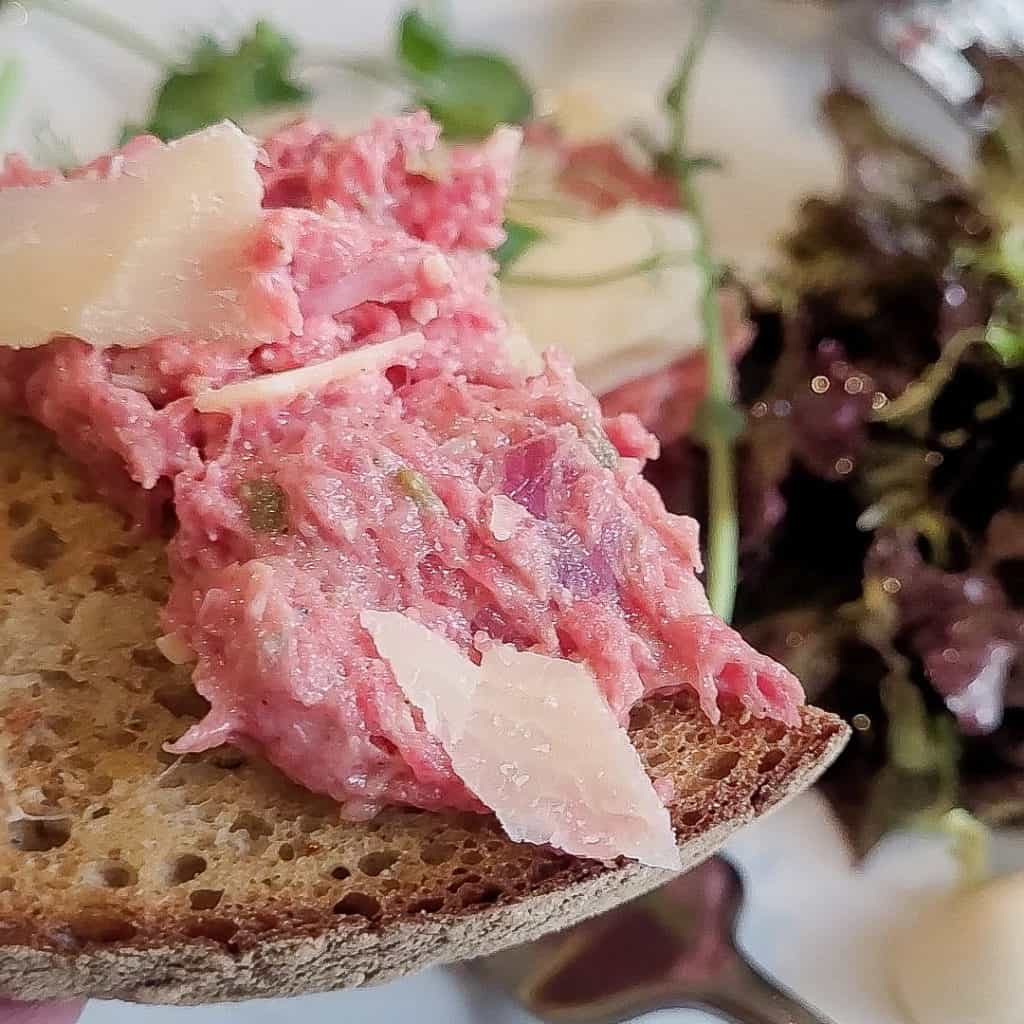 Czech beef tartare with slices of parmesan on top of toasted bread