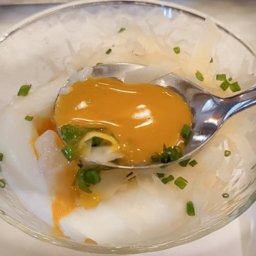 Soft boiled egg yolk on a spoon with chives and parmesan