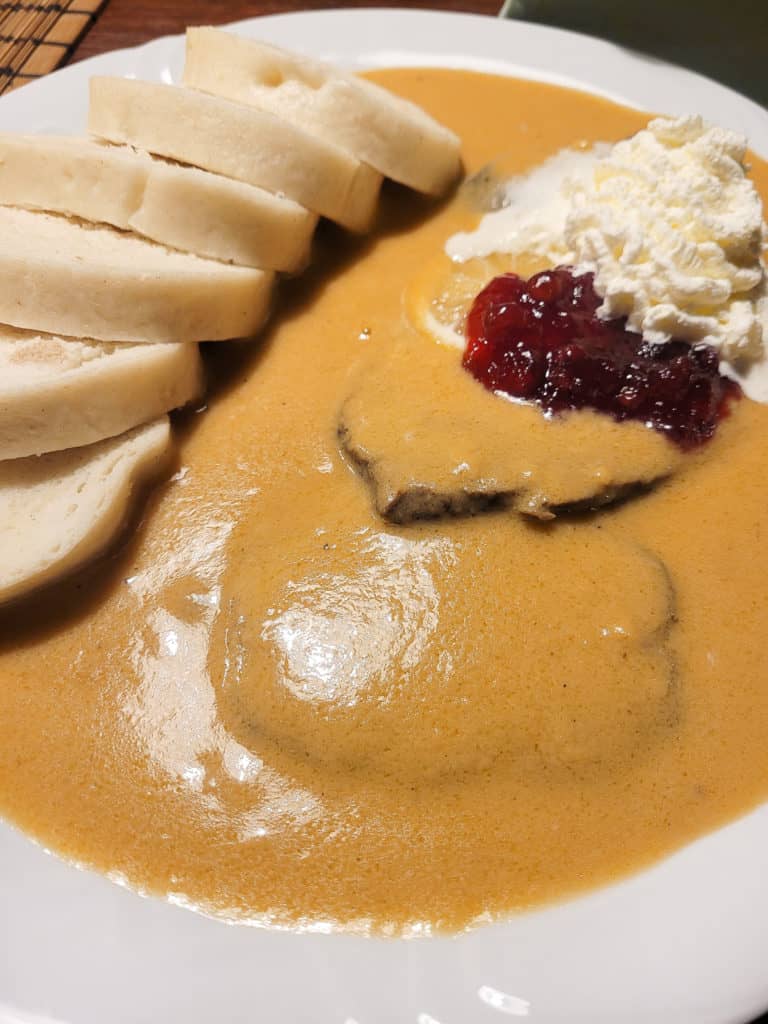 A plate of svickova with cranberry sauve, whipped cream, bread dumplings, and cream sauce.