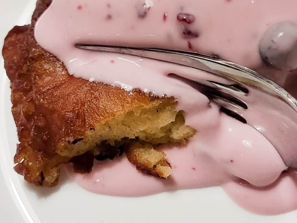 Closeup of an apple fritter with a pink sour cream sauce being sliced by a fork