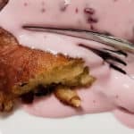 Closeup of an apple fritter with a pink sour cream sauce being sliced by a fork
