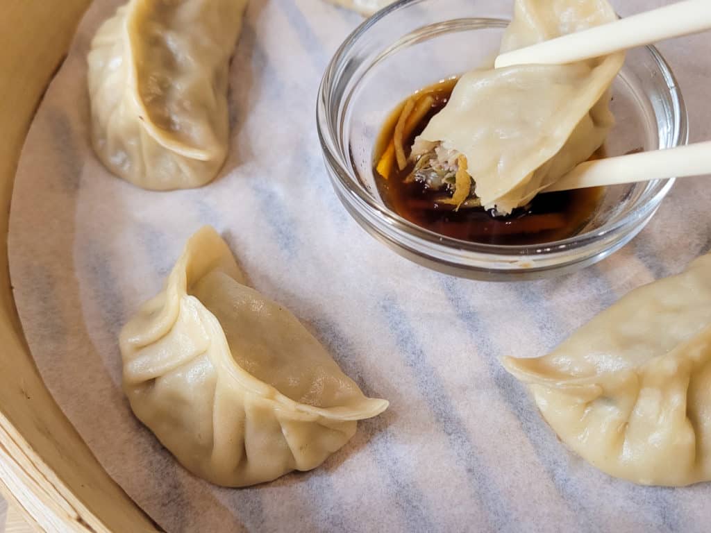 A bitten dumpling in soy sauce and vinegar surrounded by other pork and cabbage dumpling