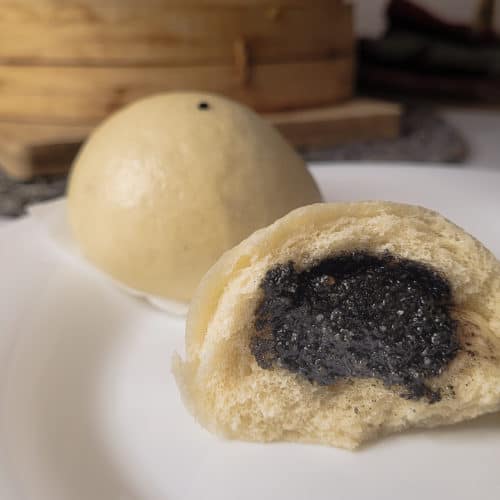 Closeup black sesame seed bun on plate with steamer basket in the background