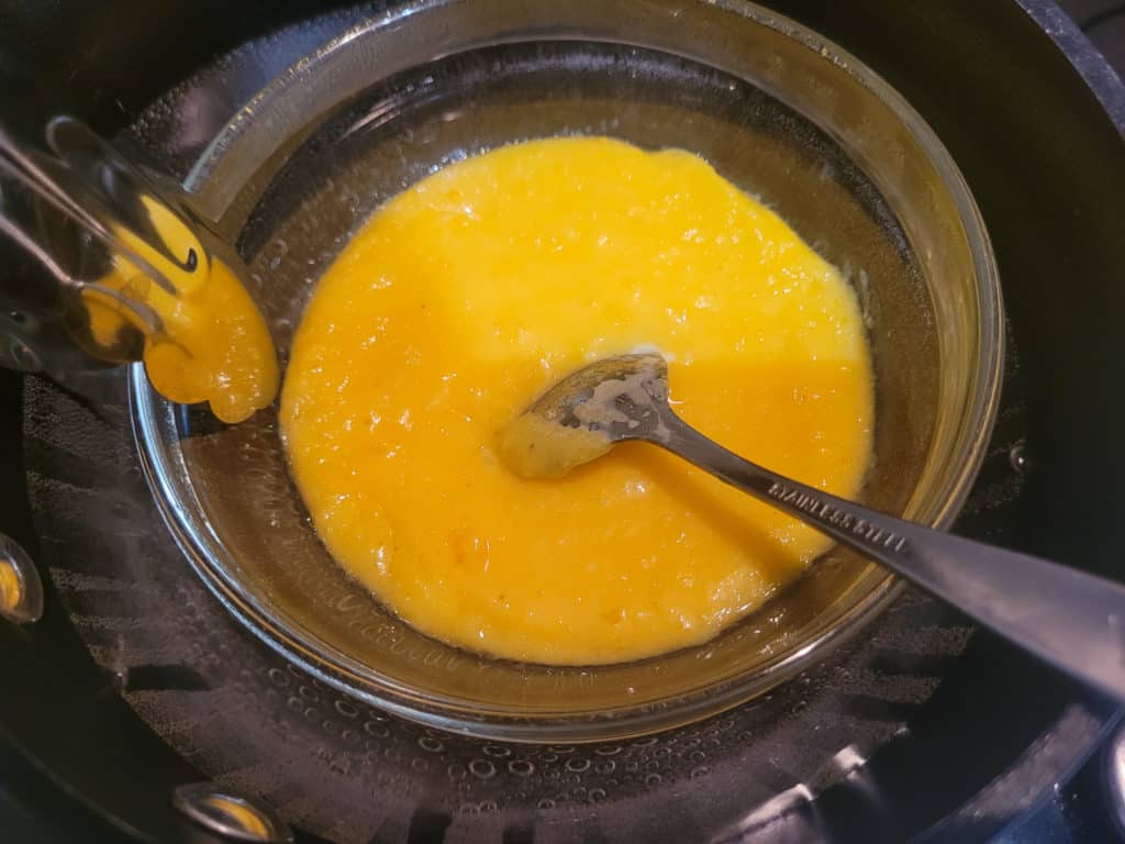 A glass bowl filled with egg yolk mixture over hot water in a pot