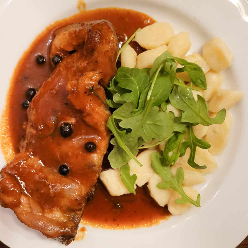 Overhead shot of pork braised in honey sauce next to potato dumplings topped with arugula