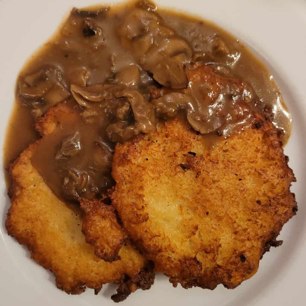 Two potato pancakes next to mushroom sauce on a white plate