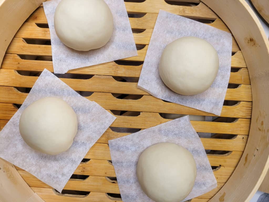 Buns on wax paper in a bamboo steamer