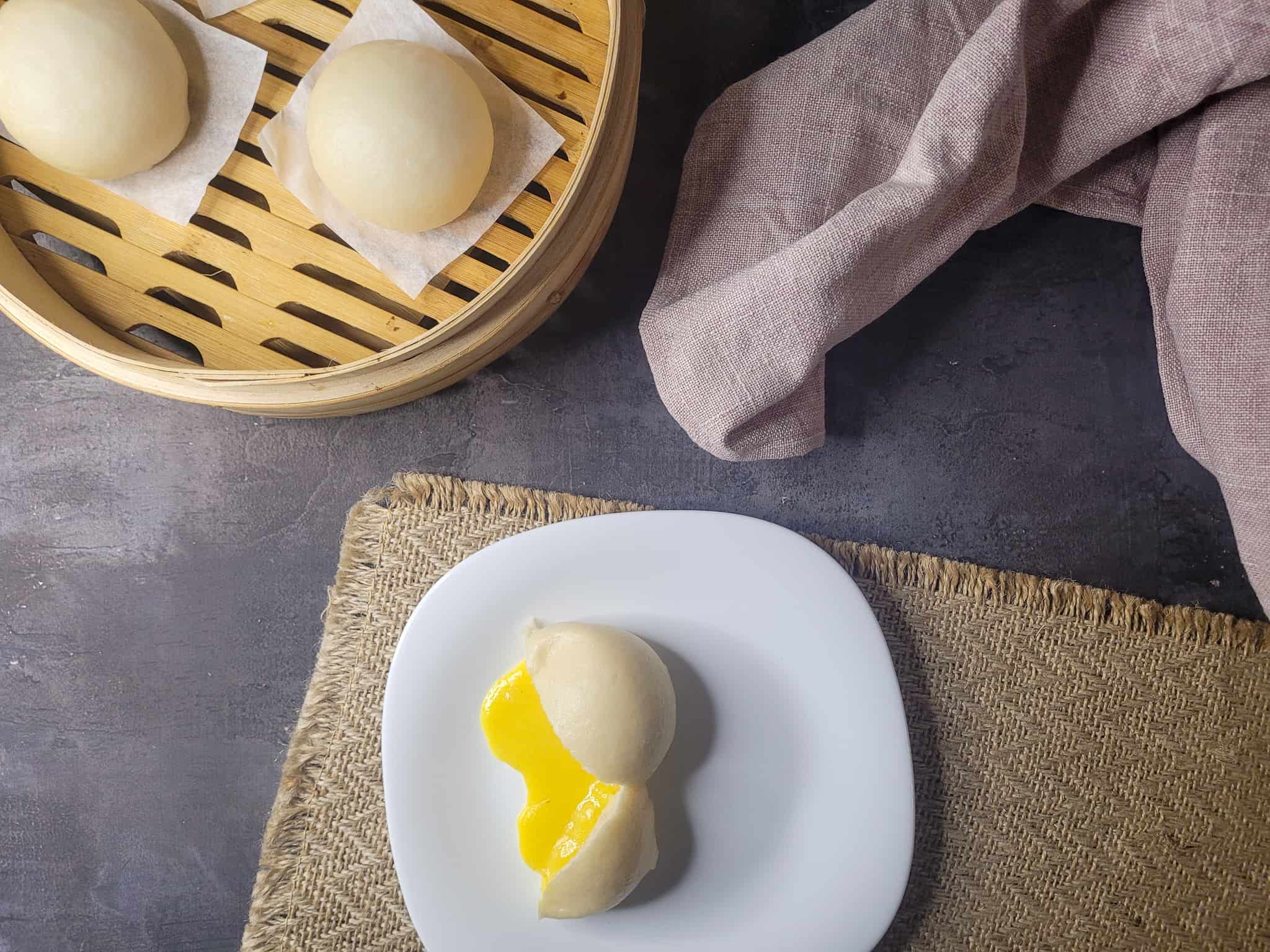 Overhead shot of salted egg yolk lava bun next to a bamboo steamer of other buns