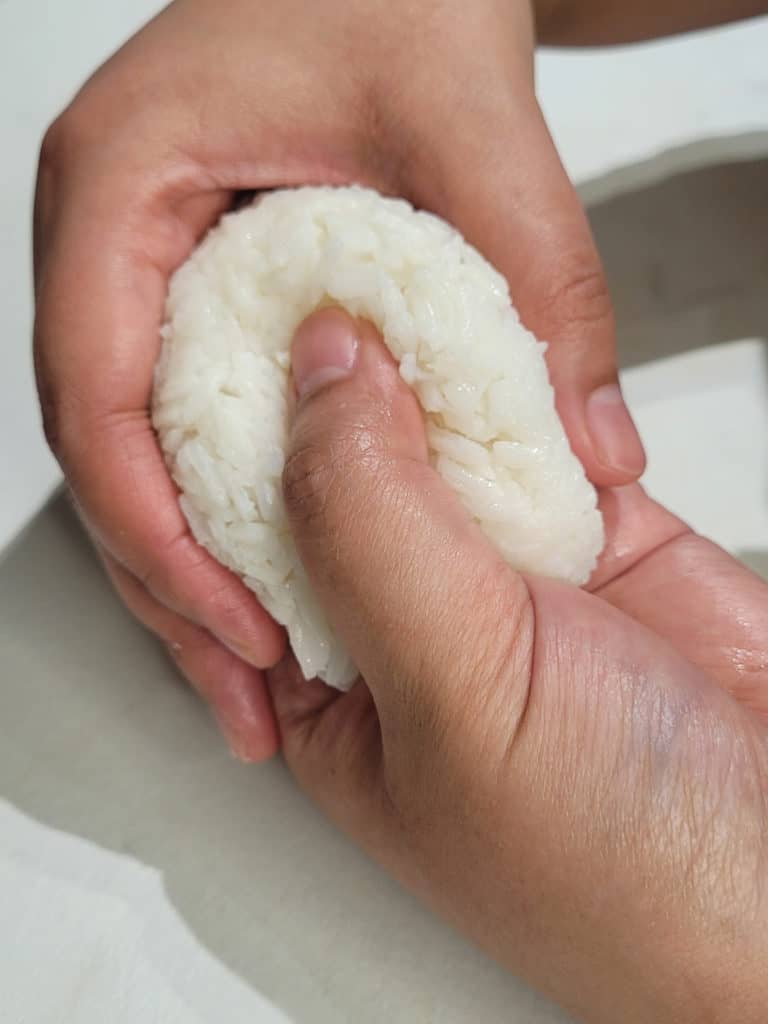 A pair of hands shaping rice with a thumb creating an indent