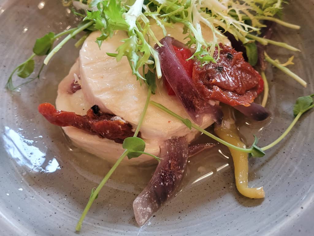 Circular slices of cheese topped with pickled vegetables in a shallow bowl