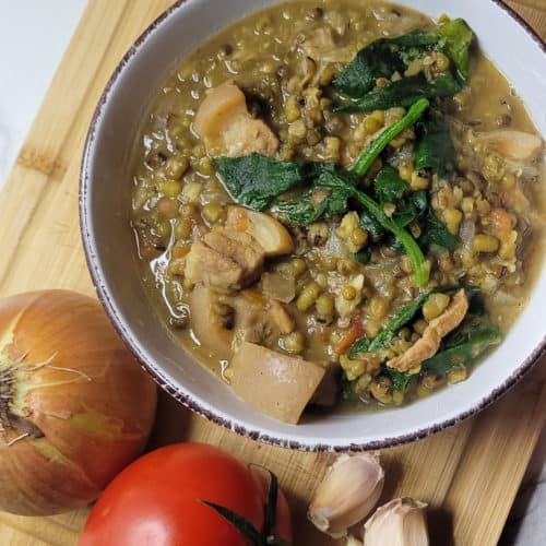 Filipino mongo in a white bowl next to an onion, tomato and some garlic cloves