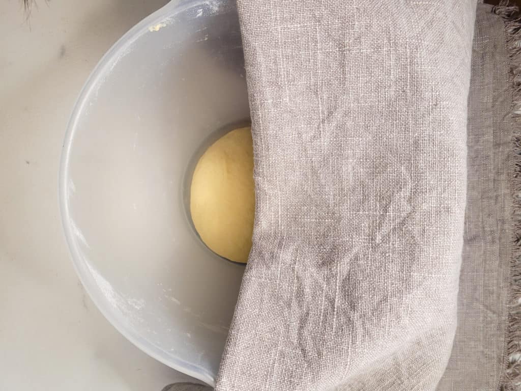 Dough in a clear bowl about to be covered with a towel