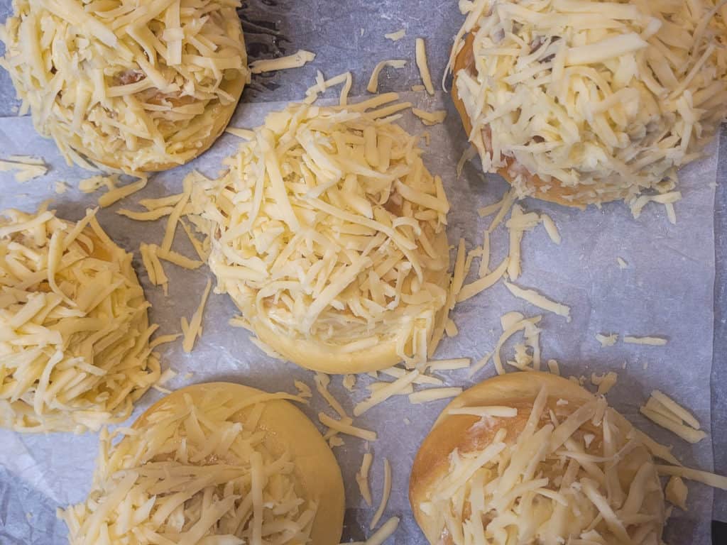 Six buns with cheese topping on a lined baking sheet