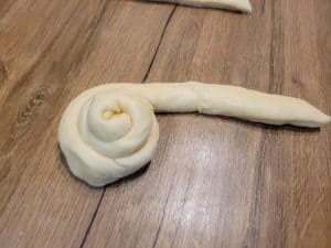 A rolled bun in progress on a wooden table