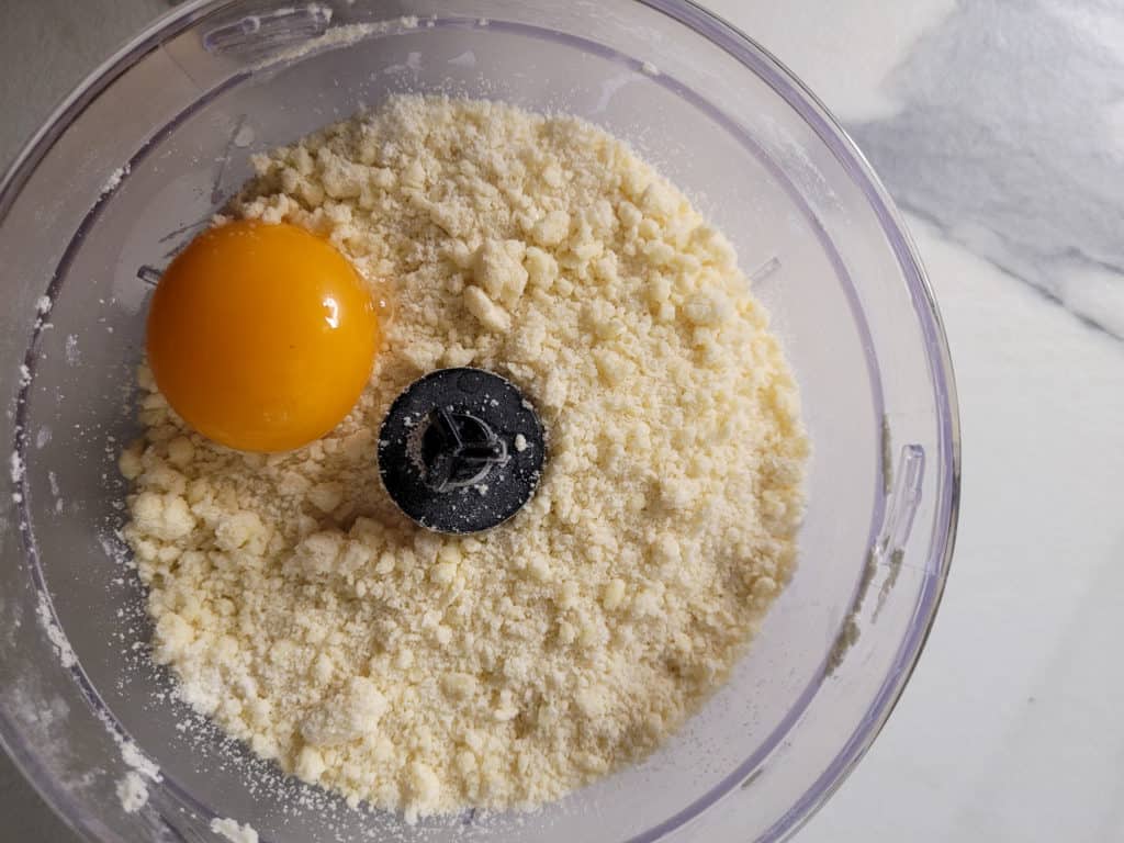 Sandy dough and an egg yolk in a food processor