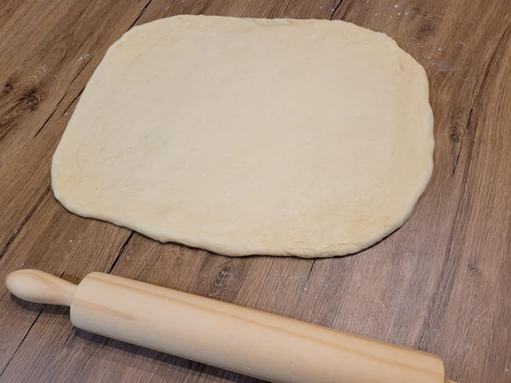 Dough shaped like a rectangle next to a wooden rolling pin