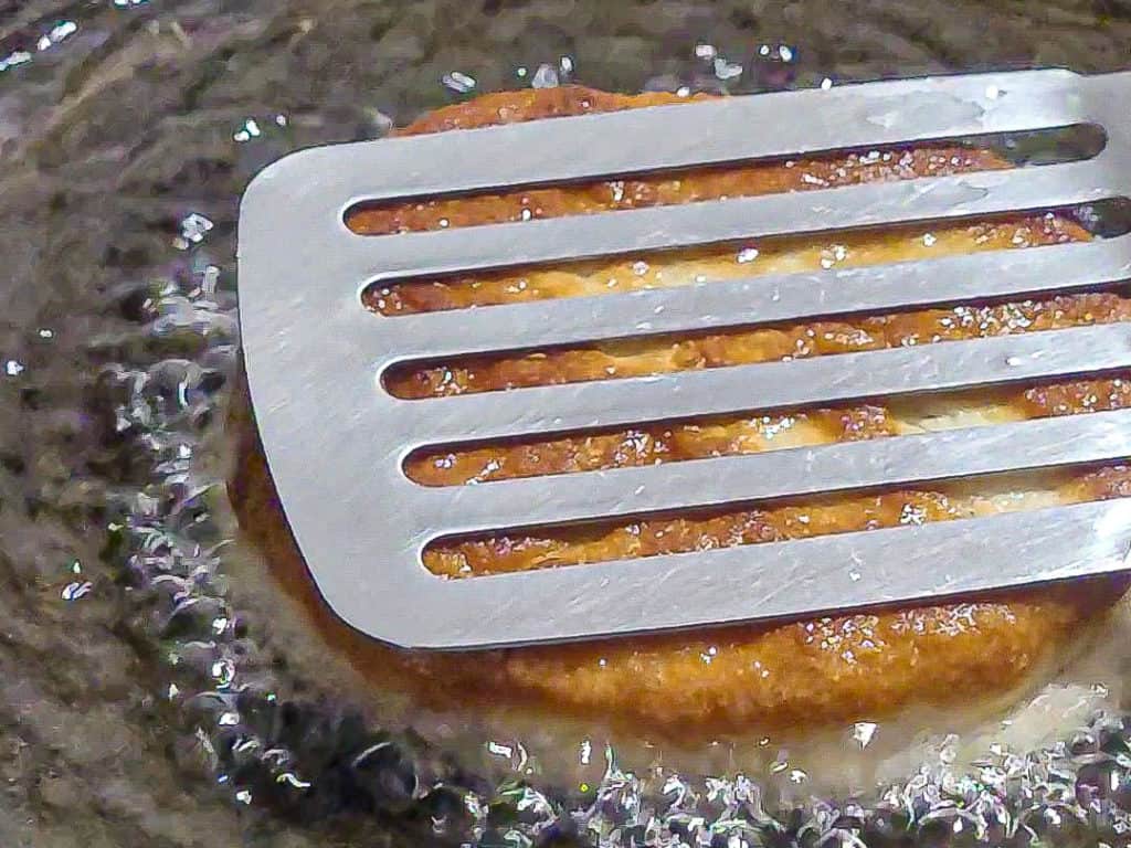 A metal spatula flattens dough frying in hot oil
