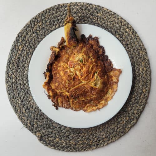 Fried eggplant with vegetables on a white plate set on a blue round mat