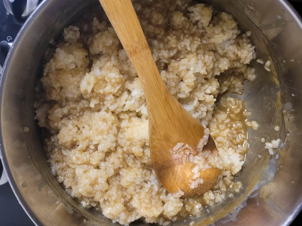 Mixing sticky rice with caramel sauce in a pot with a wooden spoon