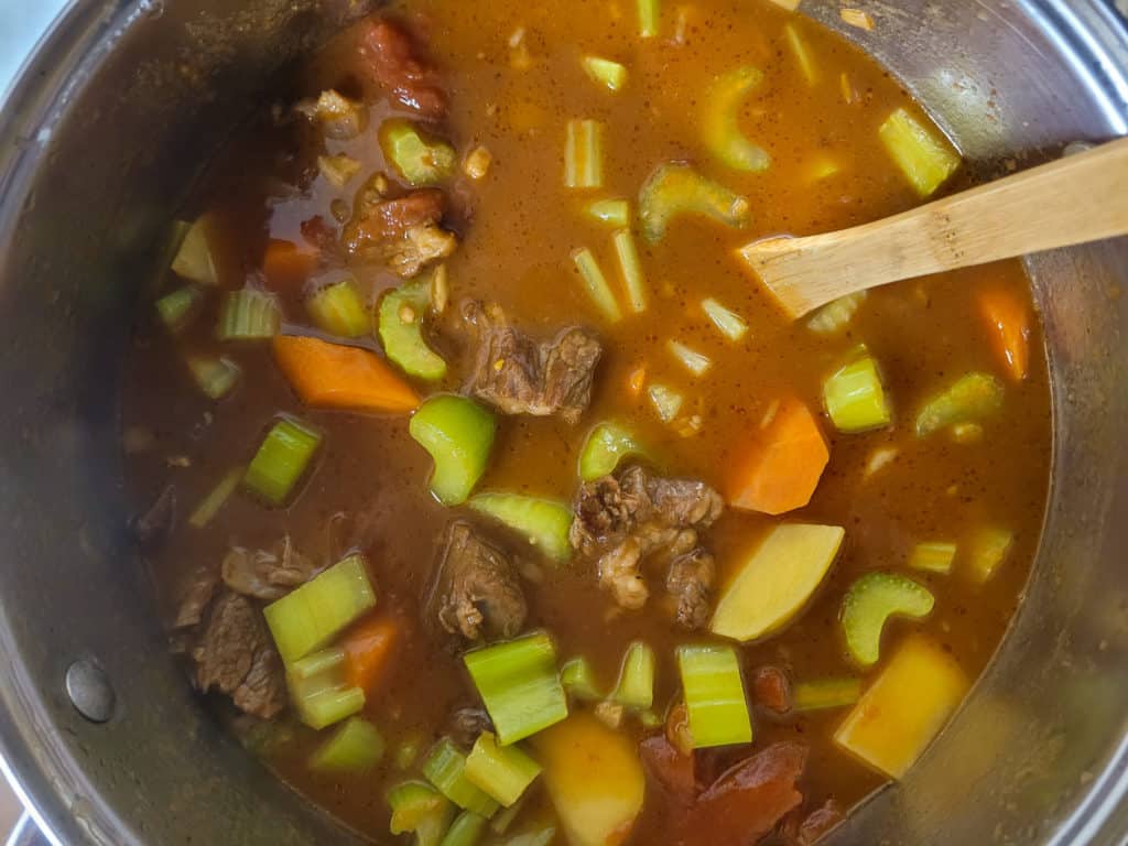 Vegetablesl and beef in a tomator sauce in a pot with a wooden spoon
