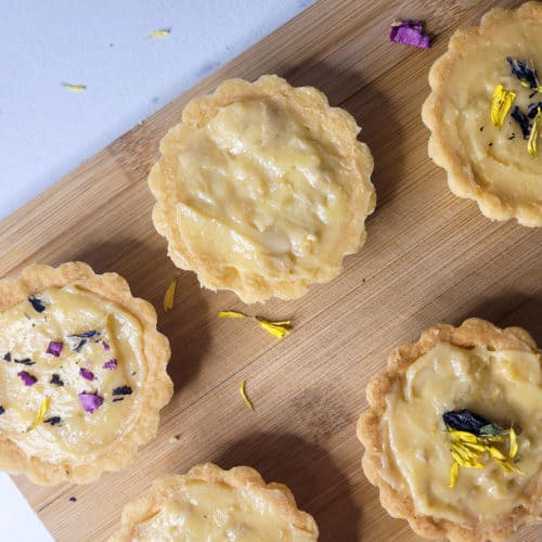 Cashew yema tarts with blue and yellow flower petals on a wood cutting board