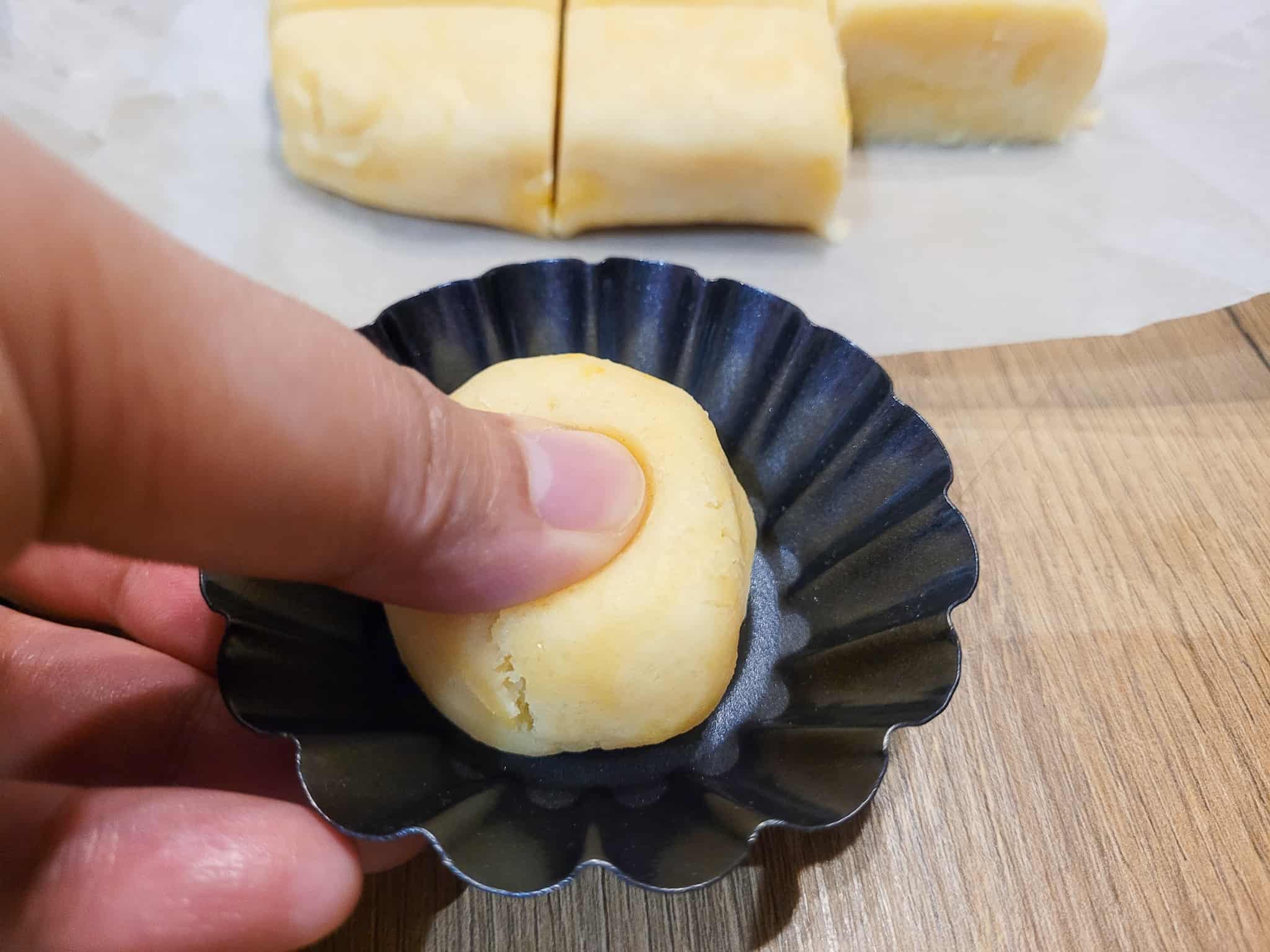 A ball of tart dough being pressed in by a thumb in a tart tin