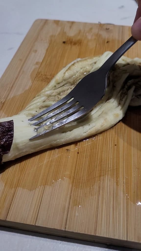 Smashing eggplant on a wooden board with a silver fork