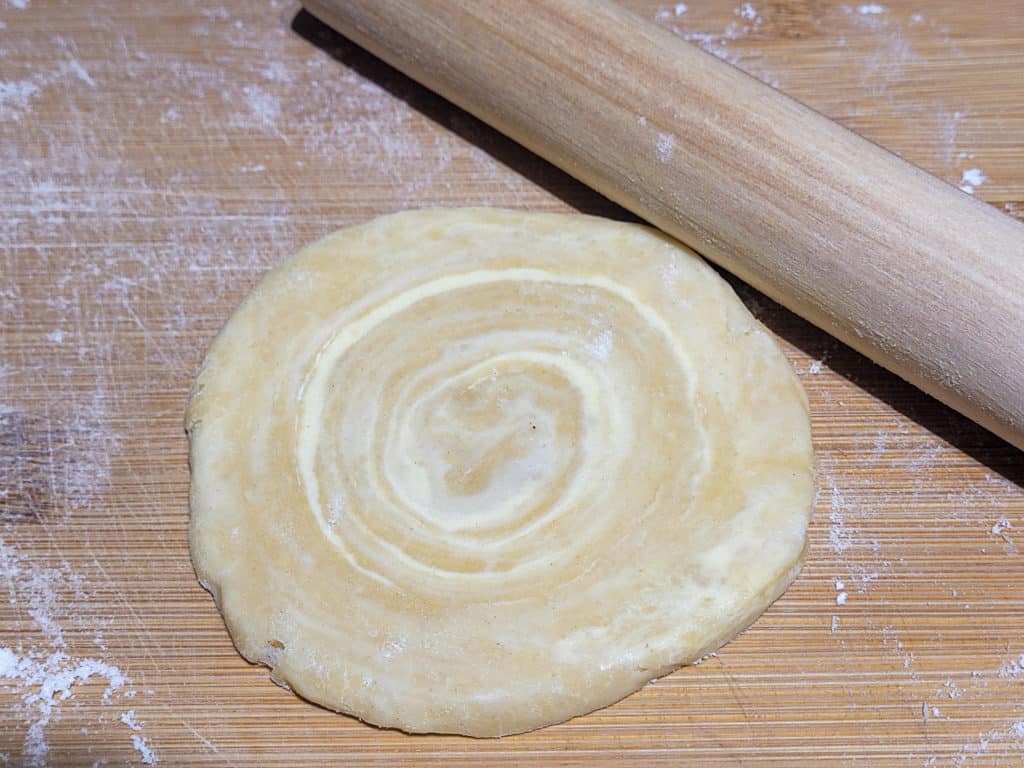 A rolled pastry dough with layers of butter next to a small rolling pin