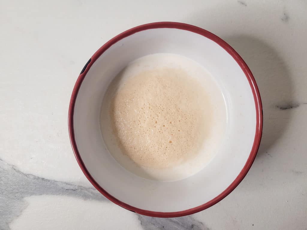 A bowl of activated yeast with milk on a white countertop
