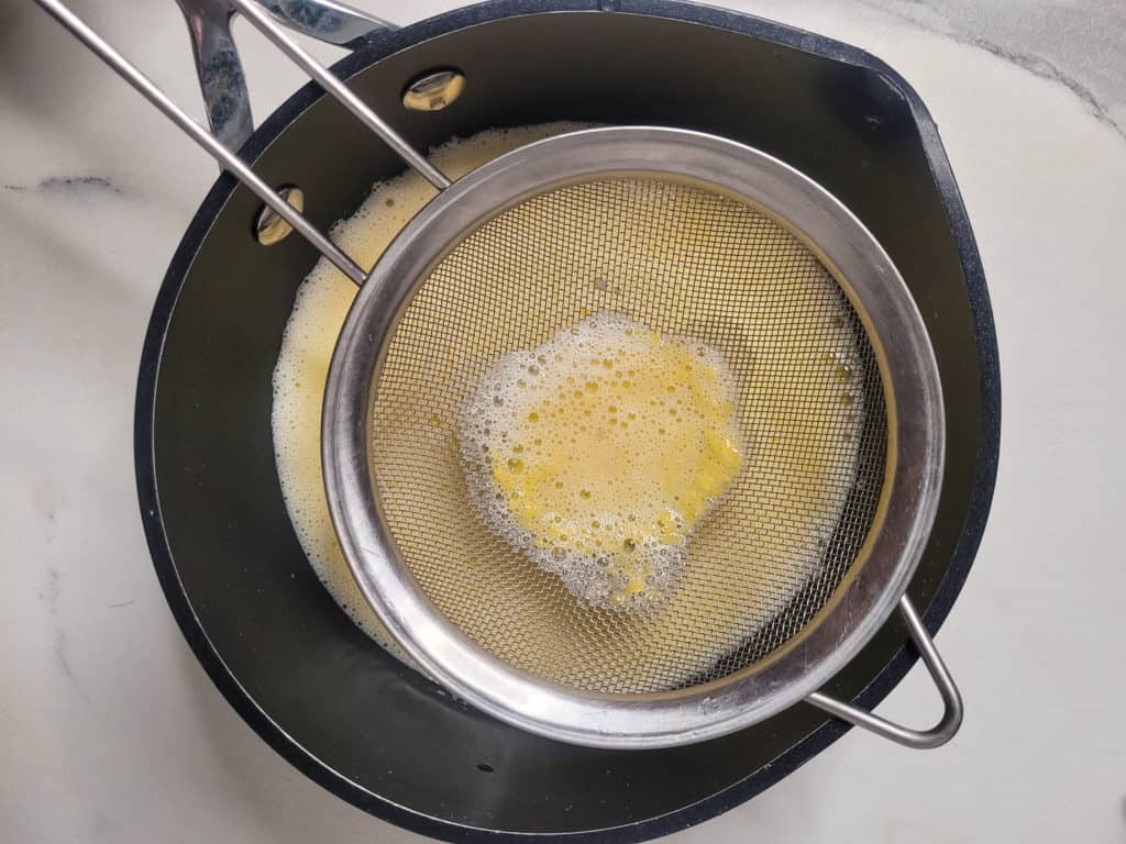 A metal sieve sitting on top of a sauce pan with custard mix