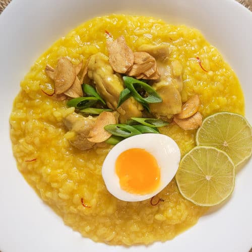 Overhead view of arroz caldo in a square white bowl on a weaved placemat