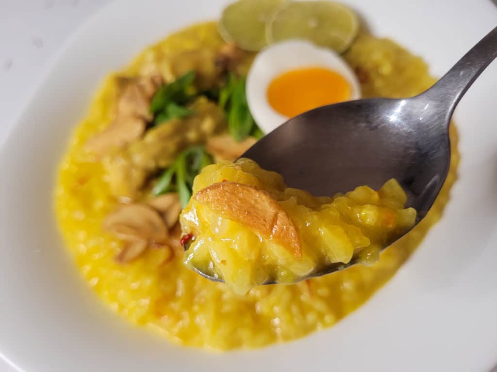 Closeup of a spoon with arroz caldo topped with a garlic chip