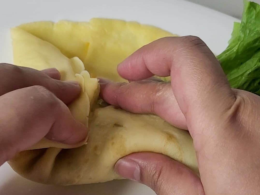 Two hands folding a crepe wrapper with lettuce