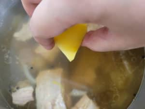 Hand placing potato into a pot of broth
