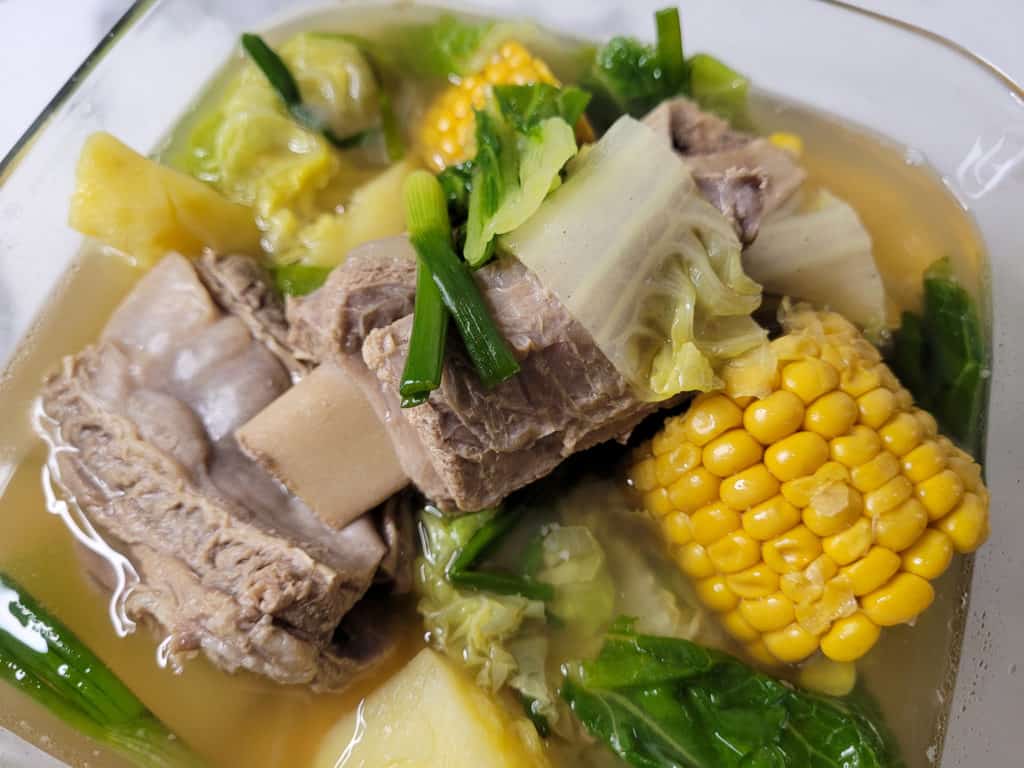 Closeup of beef ribs with corn and other vegetables in a clear bowl