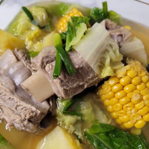 Closeup of beef ribs with corn and other vegetables in a clear bowl