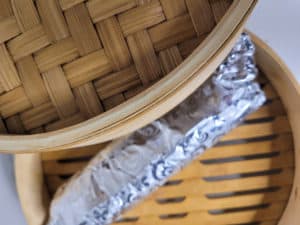 Steamed meatloaf in aluminum foil inside a bamboo steamer