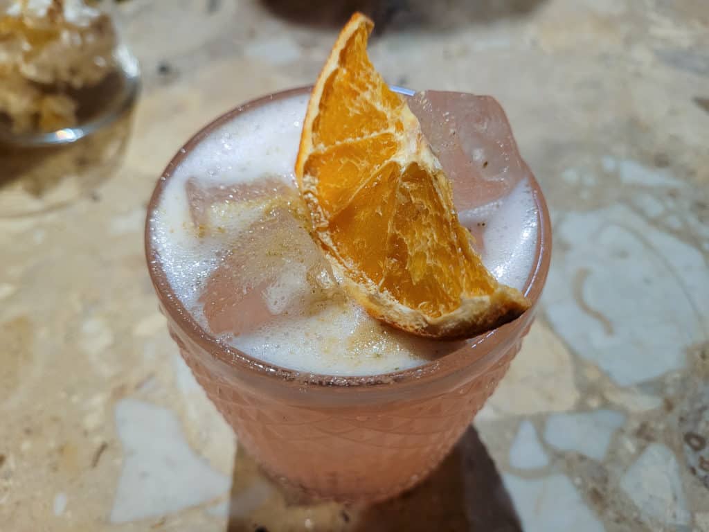A closeup of a pink cocktail with an orange garnish