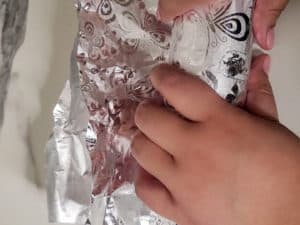 Hands rolling aluminum foil around raw meat