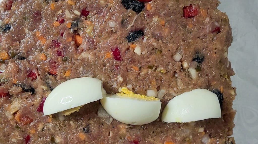 Closeup of sliced eggs on raw meatloaf on aluminum foil