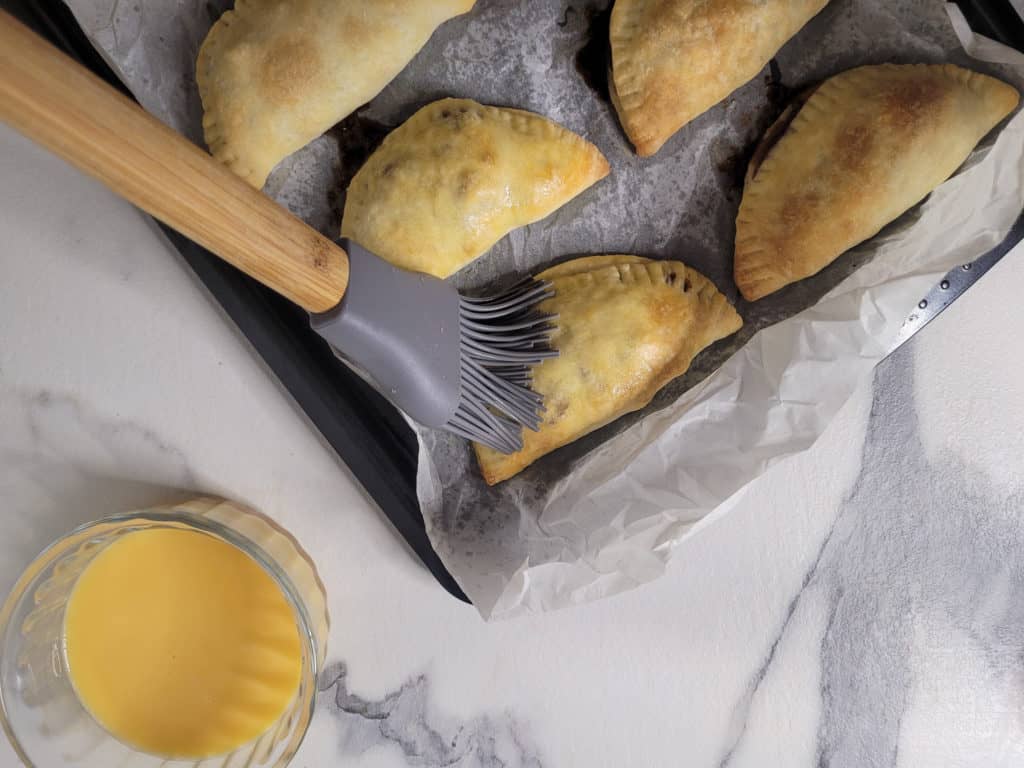 Silicone brushing egg white on baked empanadas