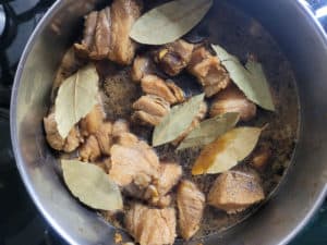 Overhead view of bay leaves in a pot of simmering adobo