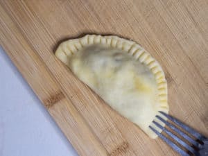 Sealing an empanada on top of cutting board with a fork